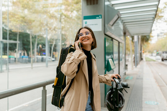 Fototapeta Smiling woman talking on mobile phone while standing at tram station in city
