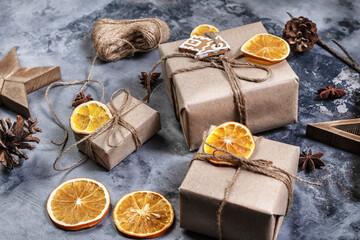 Wrapping rustic eco Christmas packages with brown paper, string and dried oranges on dark background