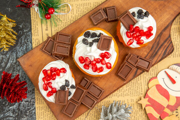 top view berry cakes and chocolates on cutting board xmas pendants on newspaper on grey-white background
