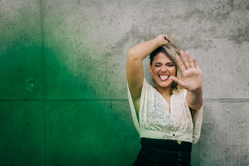 Young woman showing stop gesture while standing against green wall