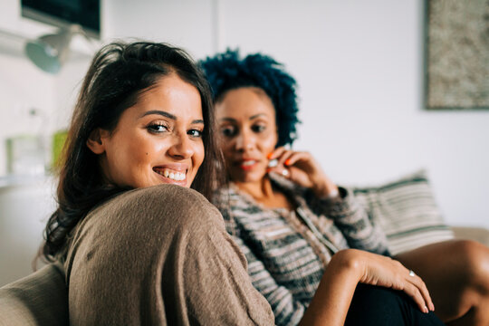 Smiling young woman with friend sitting on sofa at home