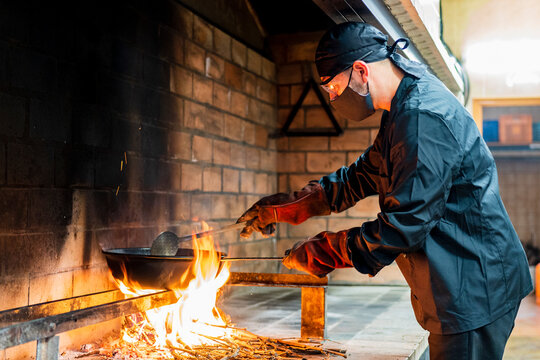 Traditional cooking of paella in restaurant kitchen, chef wearing protective mask