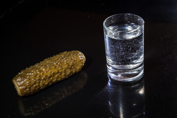 Studio shot of glass of vodka with pickled cucumber isolated on black background.