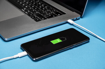 close-up of laptop charging smartphone. Phone and laptop on the table.