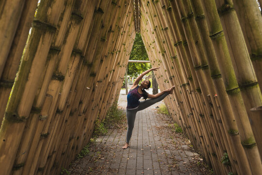 Flexible young woman stretching while leaning on bamboo covered footpath at park