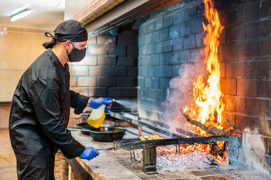Traditional cooking of paella in restaurant kitchen, chef wearing protective mask