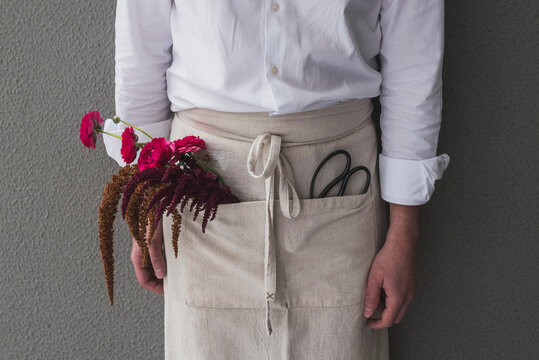 Close-up of female florist with flowers in apron standing against wall at shop