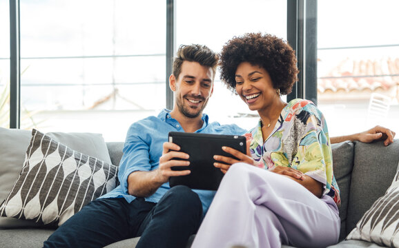 Excited diverse couple using tablet on couch