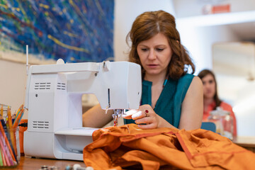 Female seamstress sewing orange fabric on machine at fashion studio