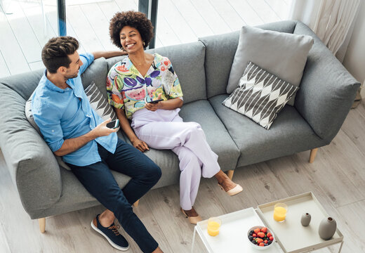 Happy interracial couple with smartphones resting on sofa - Powered by Adobe
