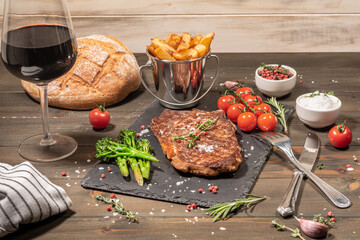 grilled rib eye steak with cherry tomatoes, broccoli and handmade chips on a slate plate. bread and glass of wine on the table .