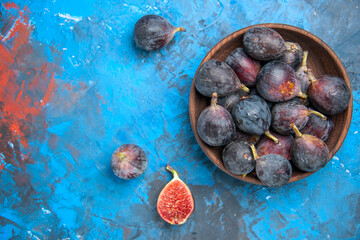 Above view of split and full fresh black mission figs in a small brown pot on blue background