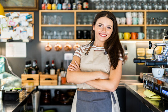 Happy female owner standing arms crossed in coffee shop