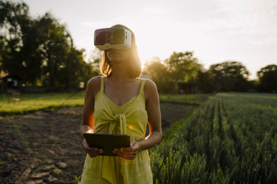 Young woman wearing VR goggles and holding tablet in a grain field in the countryside
