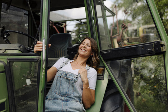 Fototapeta Cheerful young woman at a tractor in the countryside