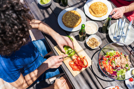 Young man cutting bell pepper at table during brunch