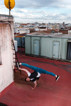 Stylish bboy performing a break dance stance close to green machinery in the rooftop of a building 