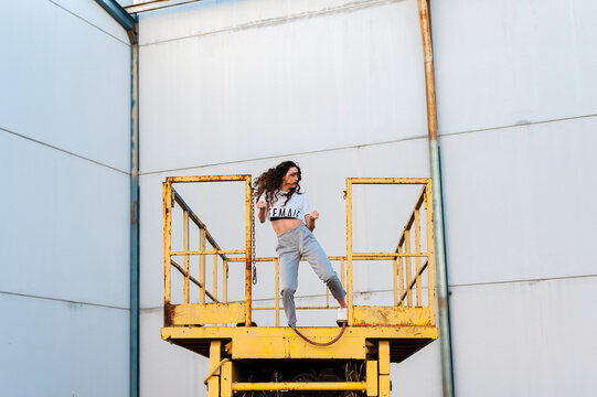 Young woman hip-hop dancer dancing at the top of an abandoned yellow crane