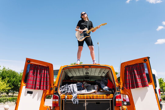 Young woman playing guitar, standing on open van