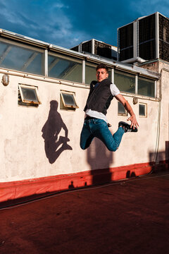Stylish bboy performing a break dance jump showing his shadow in a white wall in the rooftop of a building 