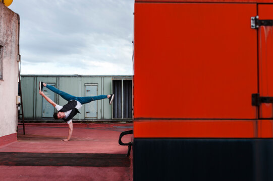 Stylish bboy performing a break dance stance close to red and green machinery in the rooftop of a building 