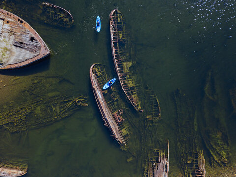 Russia, Murmansk Oblast, Kolsky District, Teriberka, Couple of sup surfers near shipwrecks on Barents Sea, aerial view