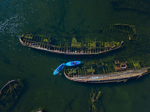 Russia, Murmansk Oblast,&not;&dagger;Kolsky&not;&dagger;District, Teriberka, Couple of sup surfers near shipwrecks on Barents Sea, aerial view