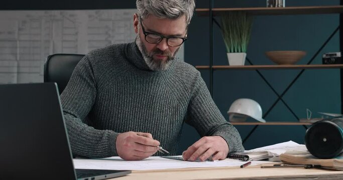 Portrait of Attractive Engineer making drawings with Pencil and ruler at his Modern Office. Looking stylish and having warm grey sweater. Serious and successful Man working at his Workplace .