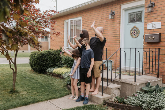 Family wearing masks waving hands while standing outside house in yard