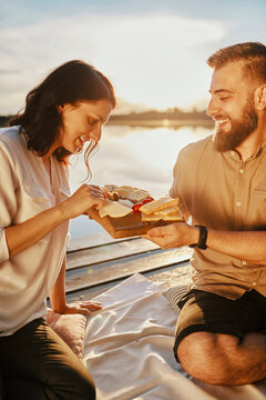 Couple having picnic on jetty at a lake at sunset eating cheese