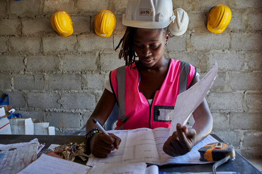 Female building contractor analyzing blueprint on desk while sitting in school