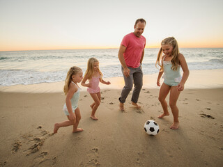 Father with children (4-5, 6-7, 8-9) playing soccer on beach