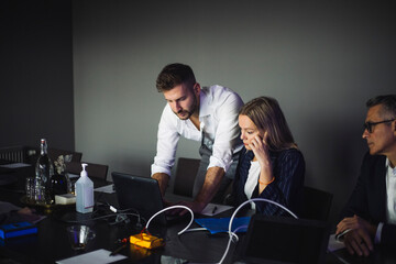 IT professional working on laptop while assisting female colleague at workplace