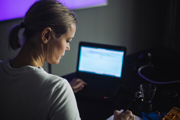 Female IT professional writing while working on laptop in creative office