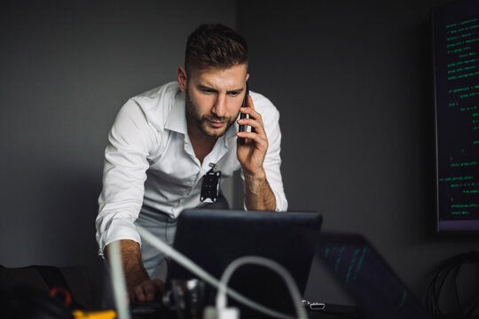 Contemplating IT professional working while talking on smart phone in creative office