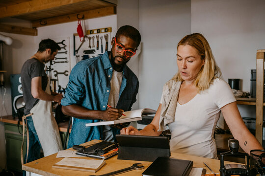 Male and female owner looking at digital tablet while colleague working in bike workshop