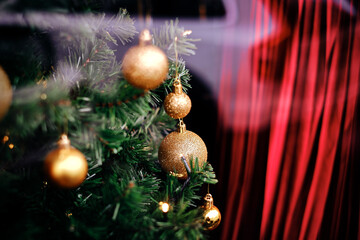 Magical green pine branches with traditional, shiny, golden christmas ornaments and a red blurred curtain in the background. Close-up shot of an X-mas tree for a wallpaper, poster, holiday card.