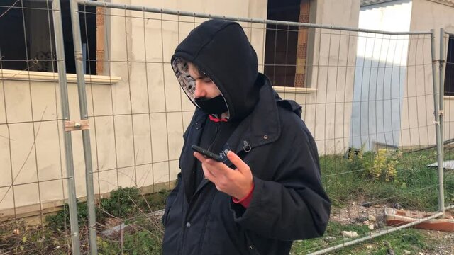 Teennager Boy in hooded top and
in medical mask using phone and walking, 