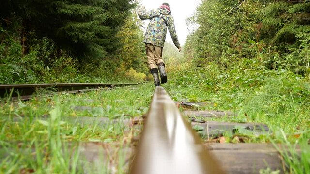 A man walks on the railroad tracks keeping his balance. Curved rails. The road in the forest