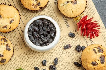 Tasty small cupcakes black raisin and accessories on newspaper on dark isolated background