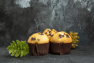 Side view of delicious freshly baked small cupcakes with chocolate and accessories on dark background