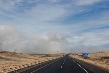 A beautiful landscape with a highway along which cars and trucks drive, on a sunny autumn day among the mountains, a blue sky with fluffy gray-blue clouds. Oregon, USA, 12-5-2019