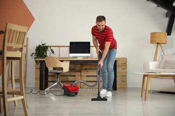 Young man using vacuum cleaner at home