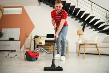 Fototapeta na wymiar Young man using vacuum cleaner in living room