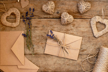 Fototapeta na wymiar festive flatly for valentine's day on wooden background. Craft paper beige envelopes decorated with lavender flowers and jute rope. Zero waste Valentine's Day concept and mock up