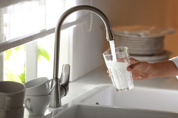 Woman pouring water into glass in kitchen, closeup