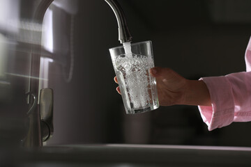 Woman pouring water into glass in kitchen, closeup