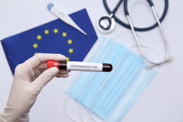Doctor holding sample tube with label Coronavirus Test above medical items and European Union flag, closeup