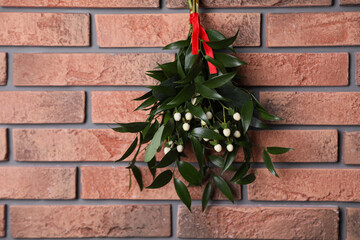 Mistletoe bunch with red ribbon hanging on brick wall. Traditional Christmas decor