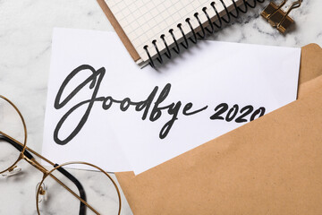 Fototapeta premium Text Goodbye 2020 written on sheet of paper on white marble table, flat lay